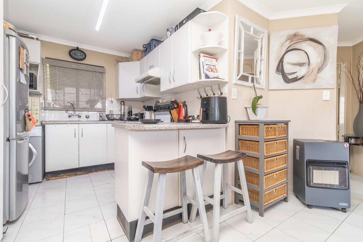 Compact kitchen featuring white cabinetry, laminate countertops, a breakfast bar, and tiled flooring, providing a functional workspace.