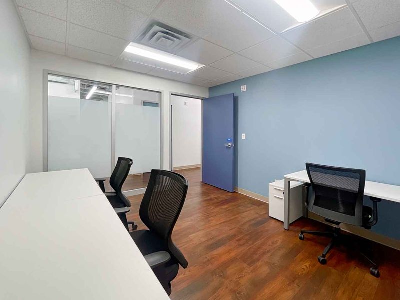 A professional office space featuring laminate flooring, a drop ceiling with recessed lighting, and a glass partition wall for an open, modern feel.