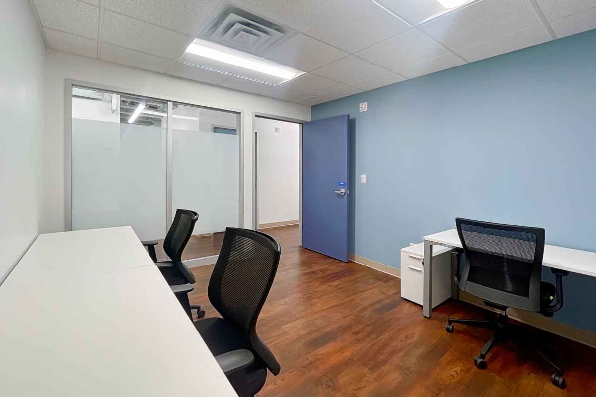 A professional office space featuring laminate flooring, a drop ceiling with recessed lighting, and a glass partition wall for an open, modern feel.