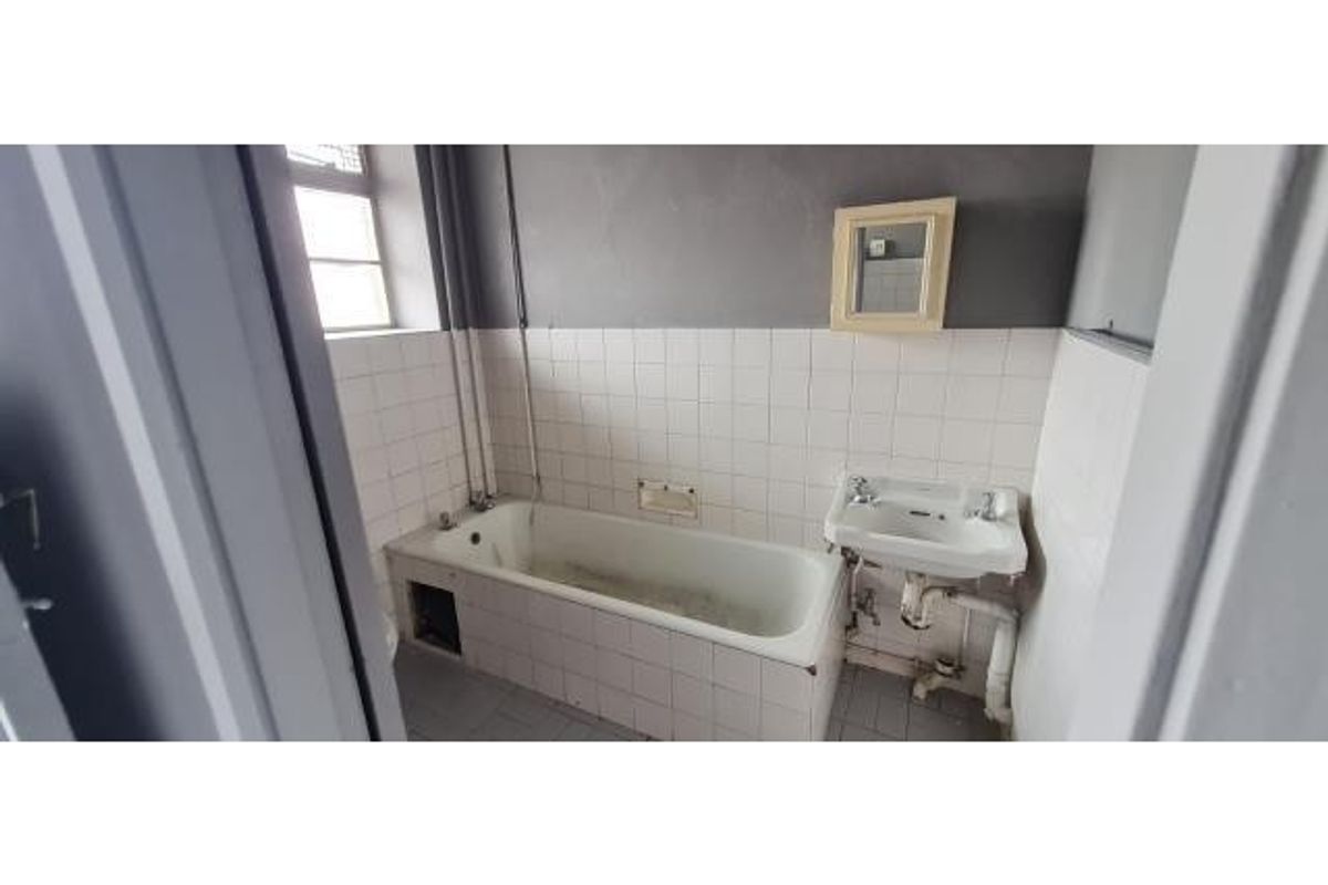 A dated bathroom featuring a standard bathtub and wall-mounted basin, requiring renovation and modernization of fixtures and finishes.