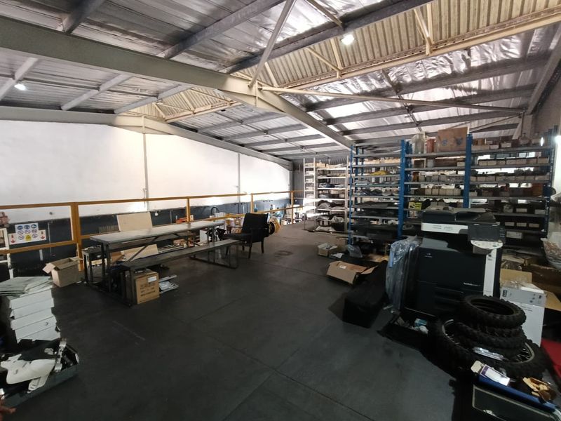 Industrial mezzanine storage area featuring exposed steel roof trusses, metal roofing, and safety railings, suitable for warehouse or workshop utility use.