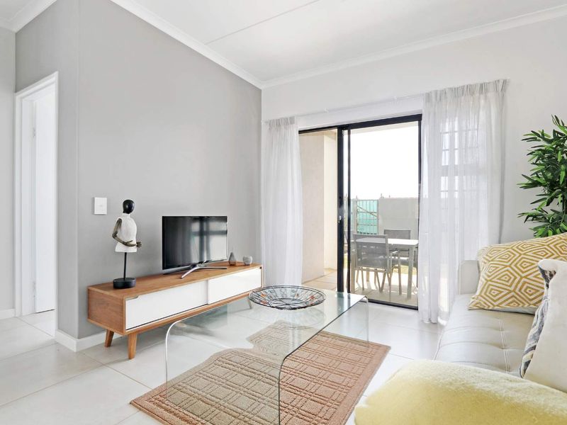 Bright living room featuring neutral tiled flooring, coved ceilings, and a large sliding glass door providing access to the outdoor patio area.