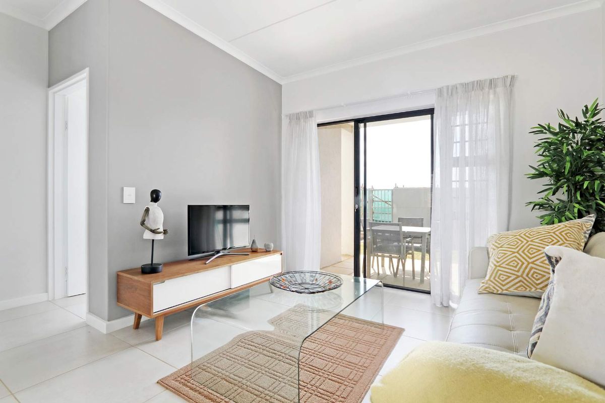 Bright living room featuring neutral tiled flooring, coved ceilings, and a large sliding glass door providing access to the outdoor patio area.