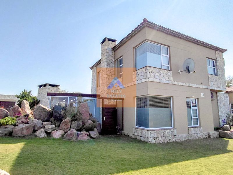 Front elevation of a two-story townhouse featuring stone cladding, corner windows, and a well-maintained lawn area.