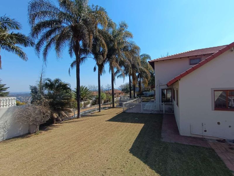 Rear exterior view of the property featuring a lawn, mature palm trees, tiled roof, and metal security fencing.