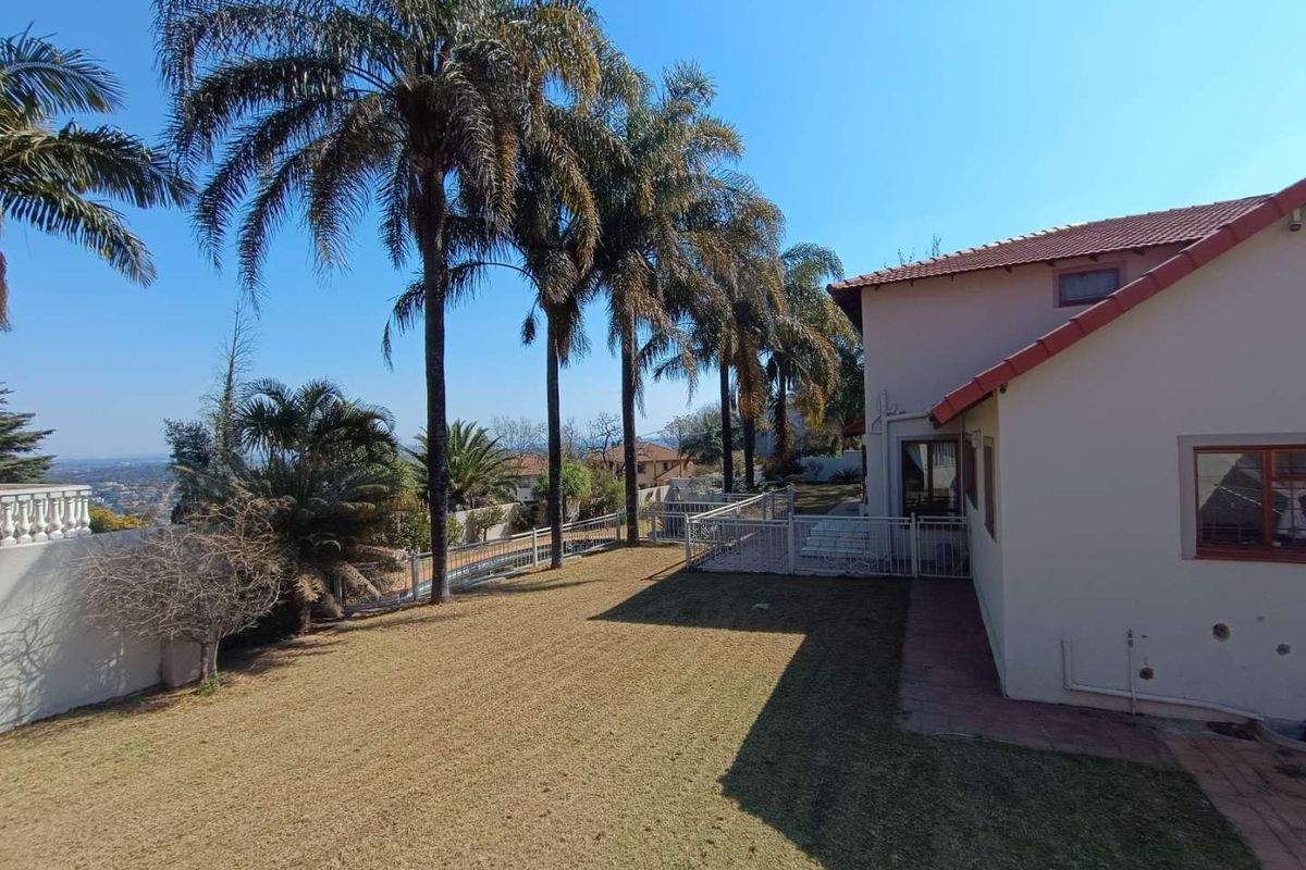 Rear exterior view of the property featuring a lawn, mature palm trees, tiled roof, and metal security fencing.