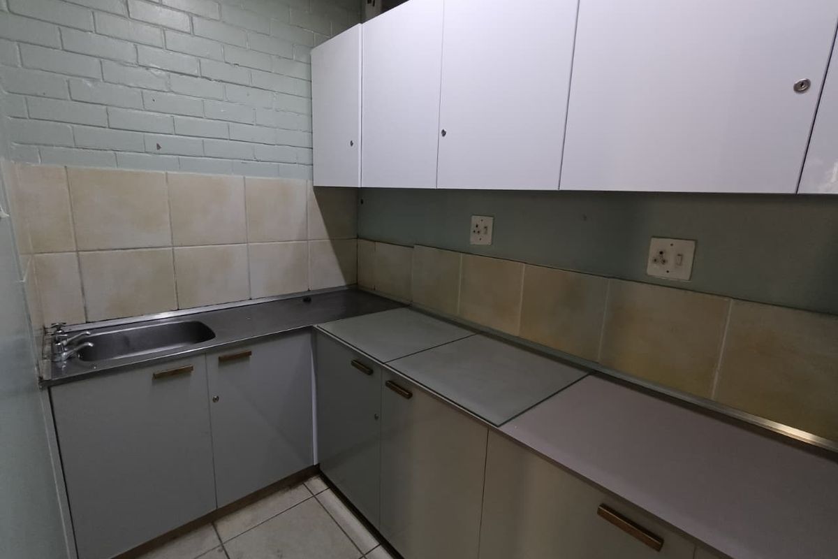 A functional kitchen area featuring built-in cabinetry, a stainless steel sink, and tiled backsplash, presenting a dated aesthetic suitable for renovation.