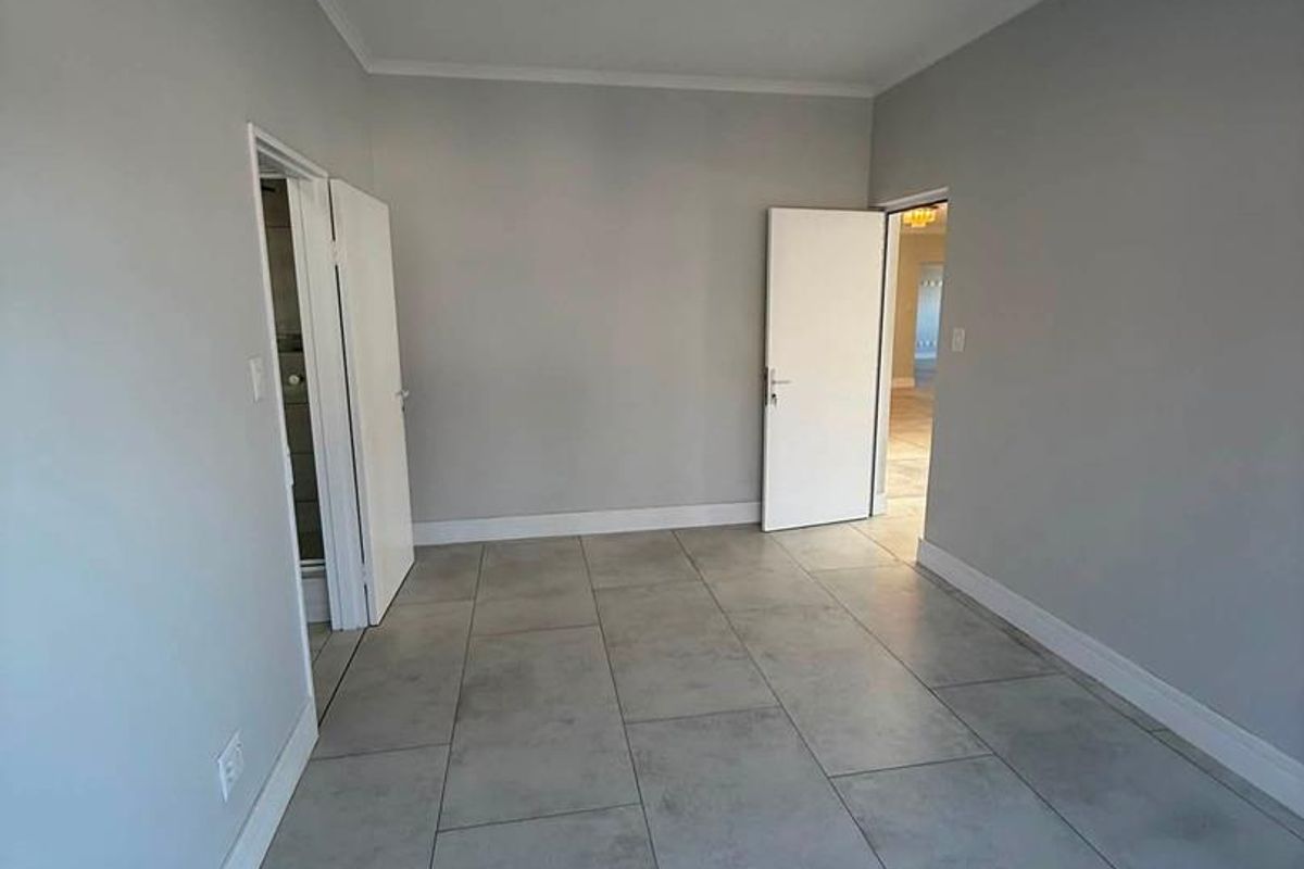 A clean, empty bedroom featuring neutral grey walls, large format floor tiles, and modern flush mount lighting.