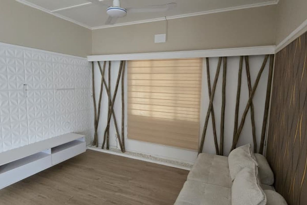 A living room featuring a wall-mounted media console, textured wall paneling, decorative timber accents, and a ceiling fan.