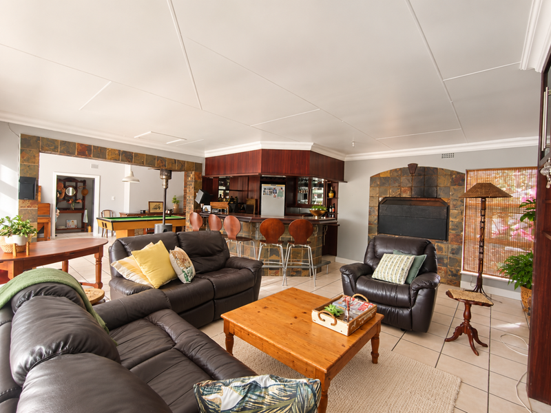 Spacious entertainment area featuring a built-in bar, stone-clad fireplace, and tiled flooring, offering a comfortable space for social gatherings.