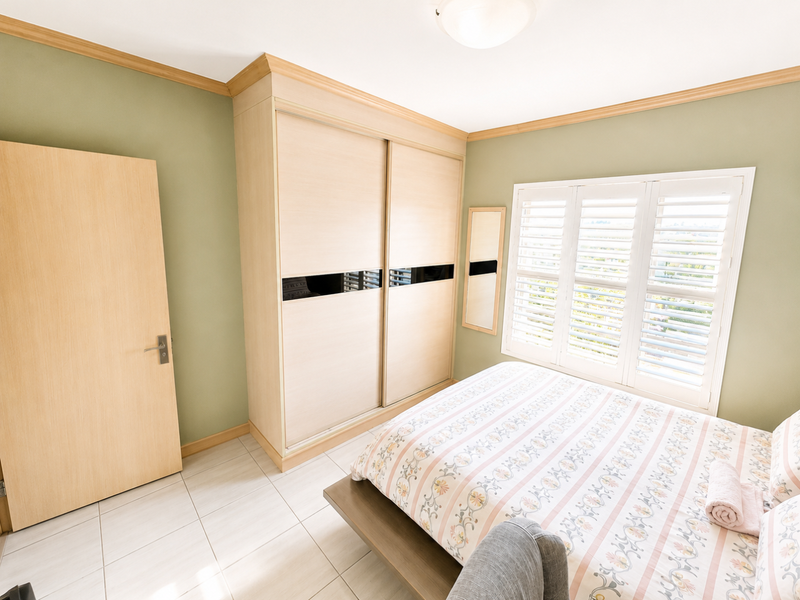 A well-maintained bedroom featuring built-in sliding door wardrobes, tiled flooring, and plantation shutters that allow for natural light.