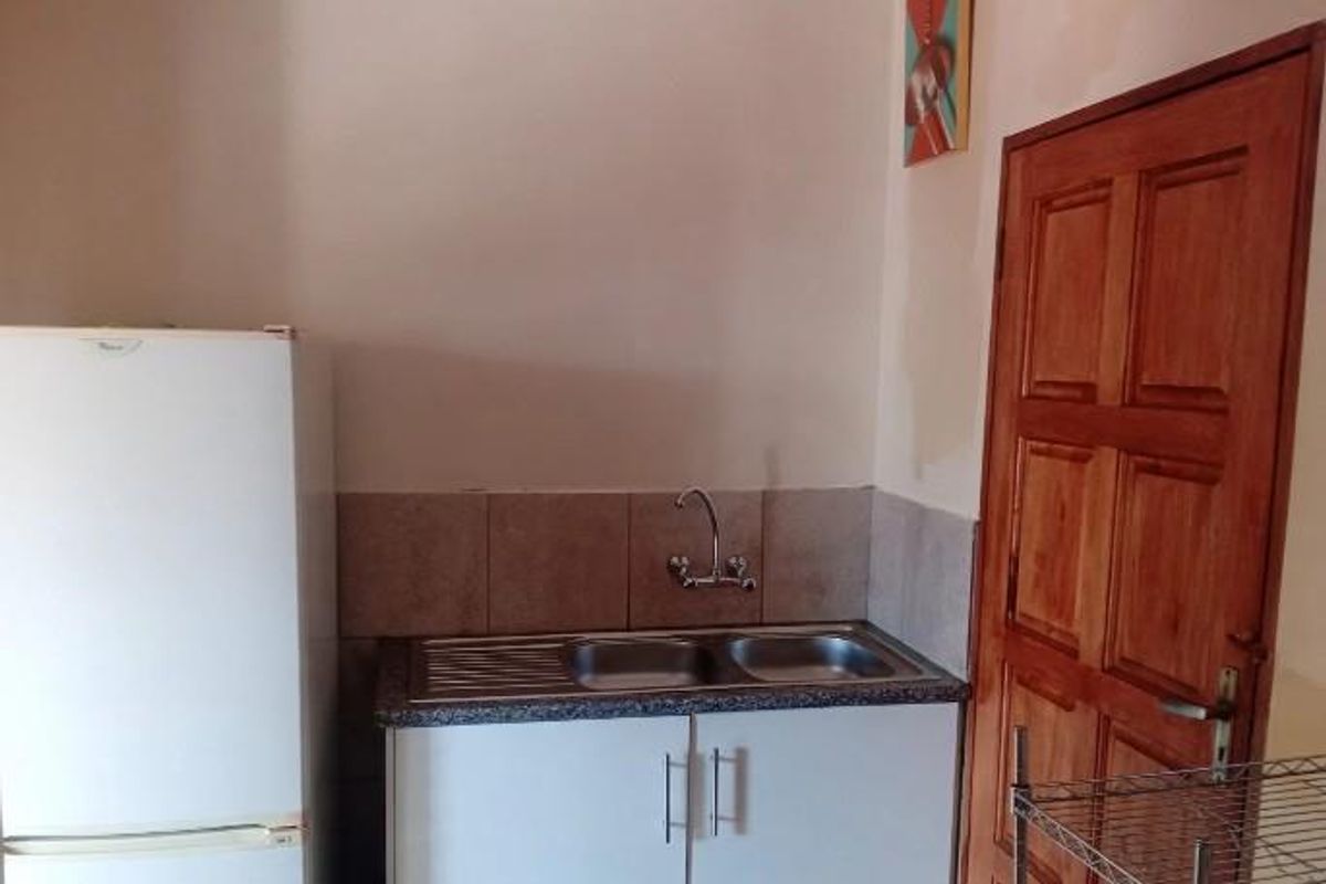 A compact kitchen area featuring a double bowl sink, tiled splashback, and functional cabinetry, with a wooden door leading to the adjacent space.