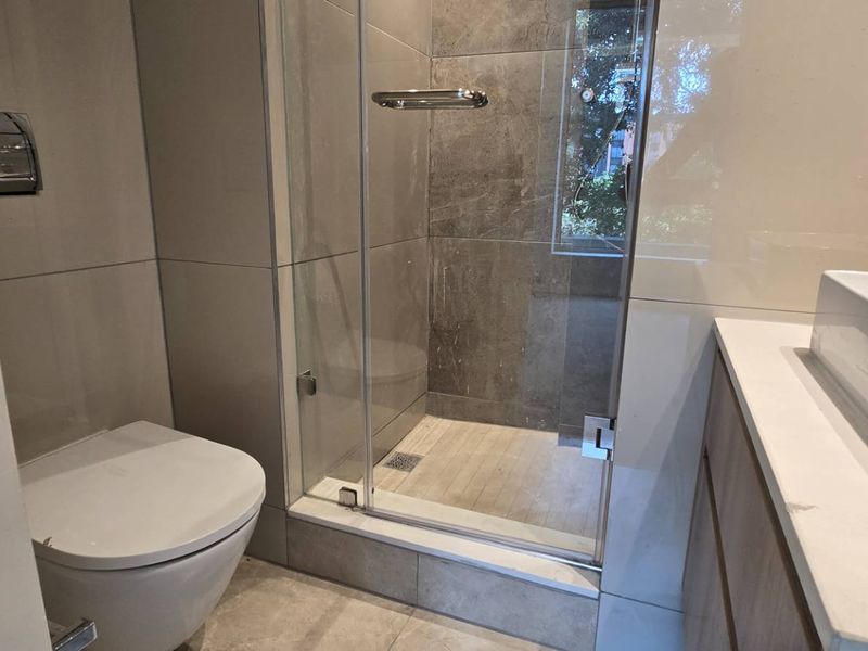 Modern bathroom featuring a wall-hung toilet, glass-enclosed shower, and a contemporary vessel sink set on a vanity cabinet with stone countertop.