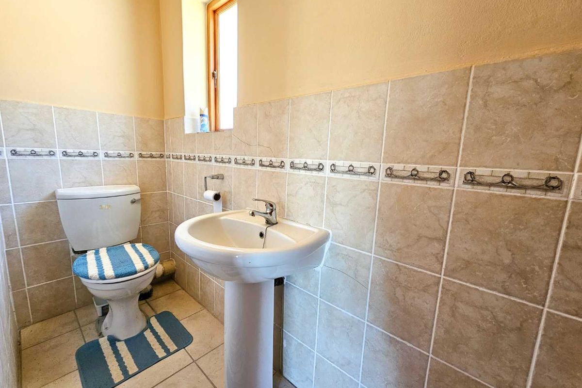 A functional bathroom featuring a pedestal basin and toilet with neutral wall tiling and a window for natural light.