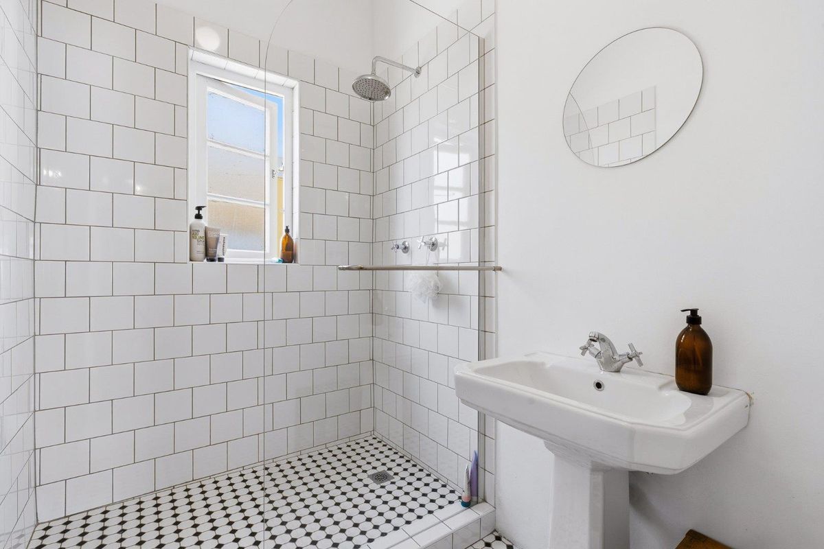 A clean, modern bathroom featuring a walk-in shower with subway tiling, mosaic floor tiles, and a classic pedestal basin.