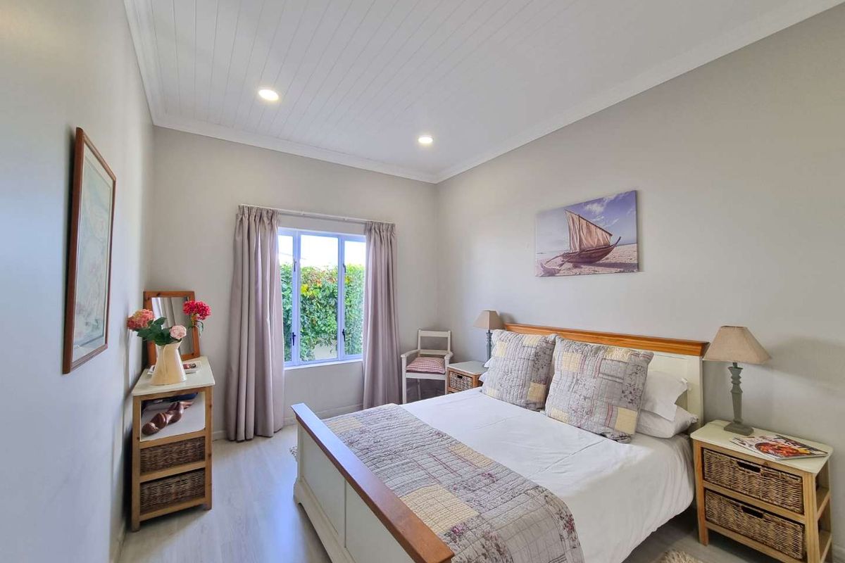 A well-maintained bedroom featuring light-toned wood-look flooring, a tongue-and-groove ceiling with recessed lighting, and a window overlooking a garden.
