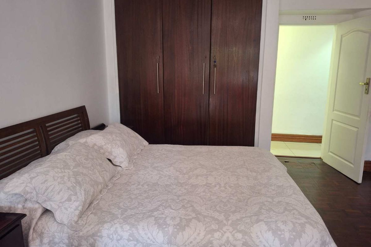 A bedroom featuring dark wood built-in cupboards and polished wooden flooring, with an adjacent hallway visible through the open doorway.