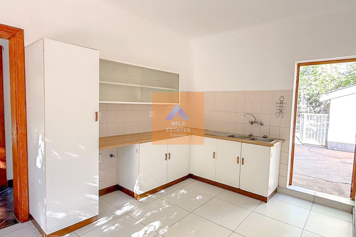 A functional kitchen featuring white cabinetry, laminate countertops, a double stainless steel sink, and tiled flooring with direct access to an outdoor area.