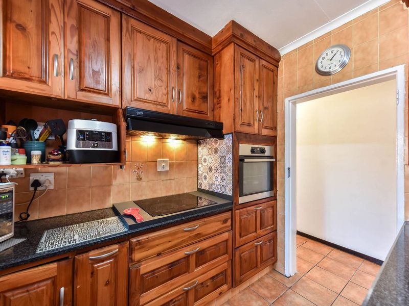 A functional kitchen featuring warm-toned wooden cabinetry, granite countertops, a built-in oven, and an electric hob with an extractor fan.