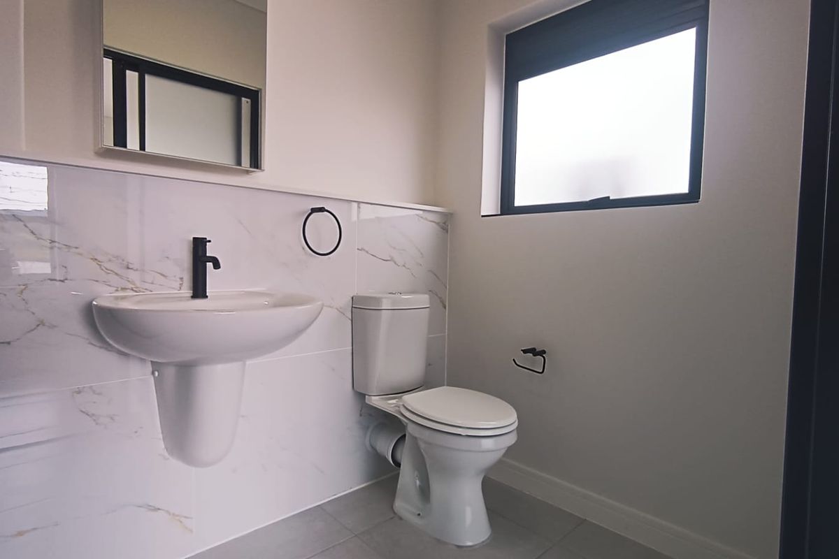 A modern, clean bathroom featuring a pedestal washbasin with a black faucet, a toilet, and elegant marble-look wall tiles.