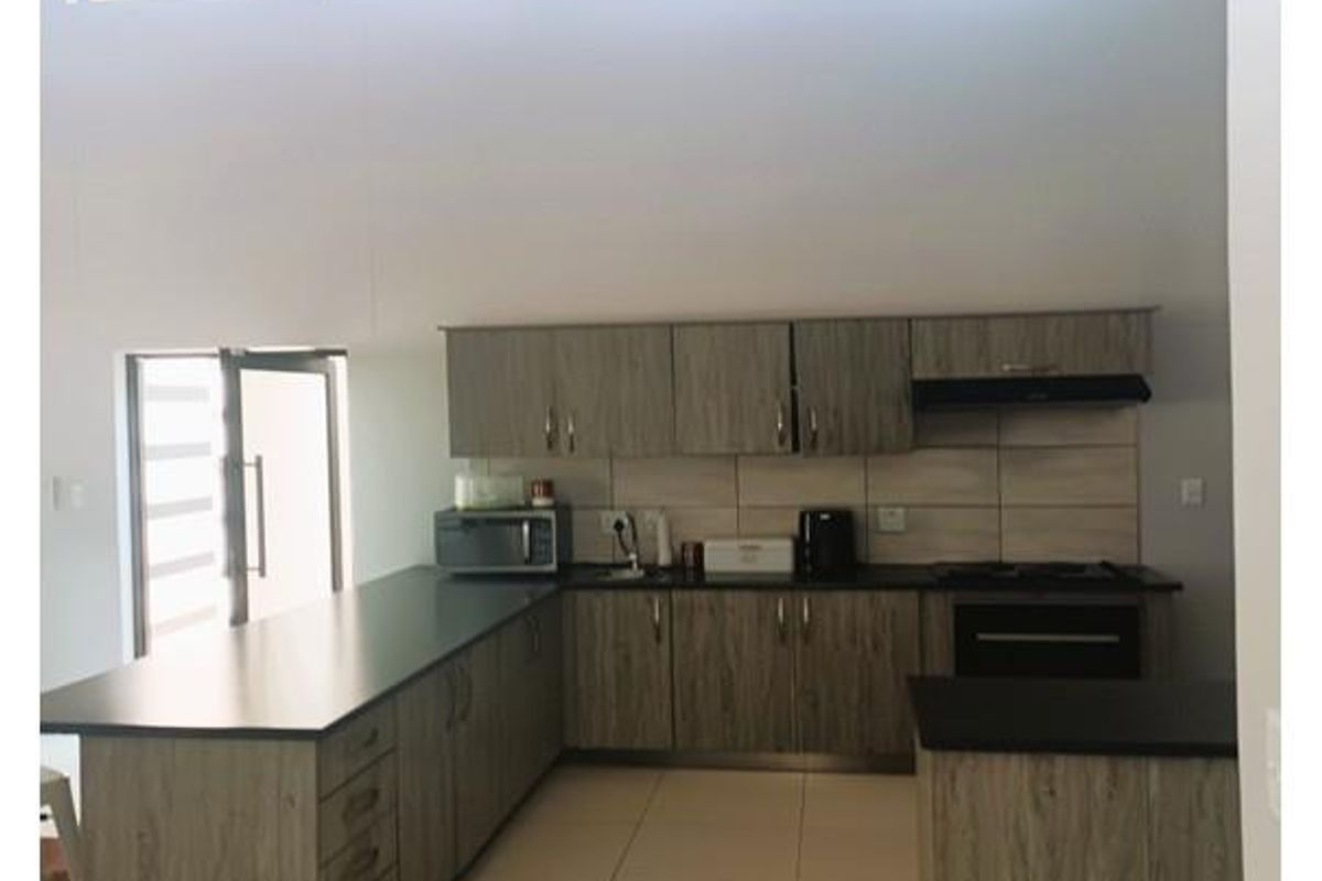 Modern kitchen featuring wood-look cabinetry, dark countertops, built-in appliances, tiled flooring, and high ceilings with exposed timber beams and clerestory windows.
