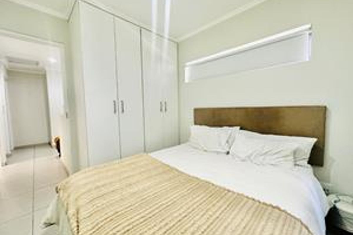 A well-maintained bedroom featuring built-in cupboards, tiled flooring, and a horizontal window with a roller blind.