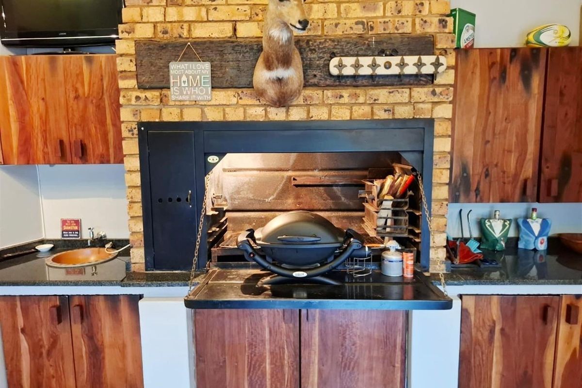 Indoor kitchen area featuring a built-in braai, granite countertops, and wooden cabinetry.