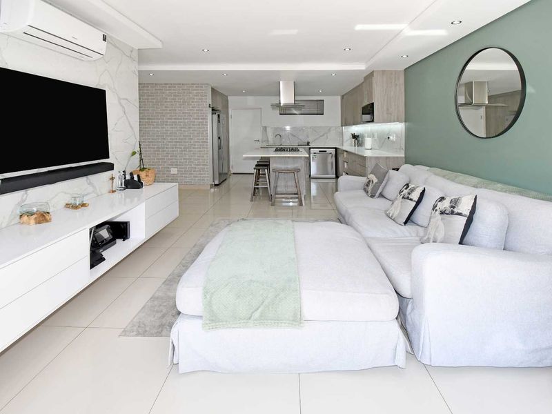 Modern open-plan living area featuring a sleek kitchen with stone countertops, island, and a marble-look feature wall with integrated air conditioning.