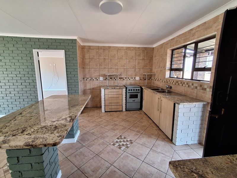 A functional kitchen featuring granite countertops, a breakfast bar, tiled splashbacks, and a freestanding stove, with a distinct brick feature wall.