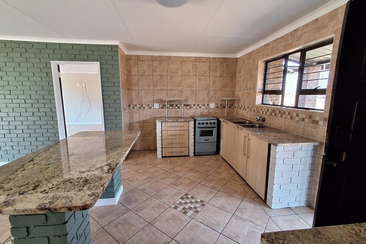 A functional kitchen featuring granite countertops, a breakfast bar, tiled splashbacks, and a freestanding stove, with a distinct brick feature wall.