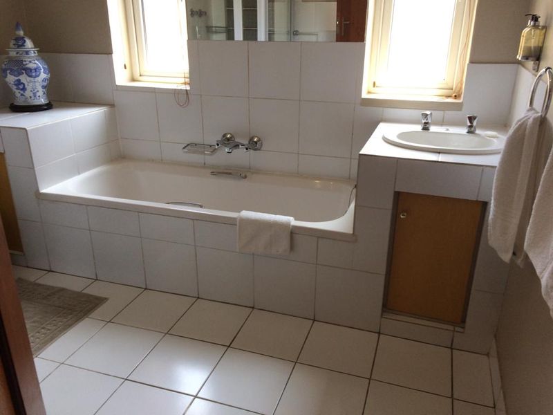A functional bathroom featuring a built-in bathtub, tiled vanity with inset basin, and neutral wall tiling, offering a classic layout ready for modern updates.