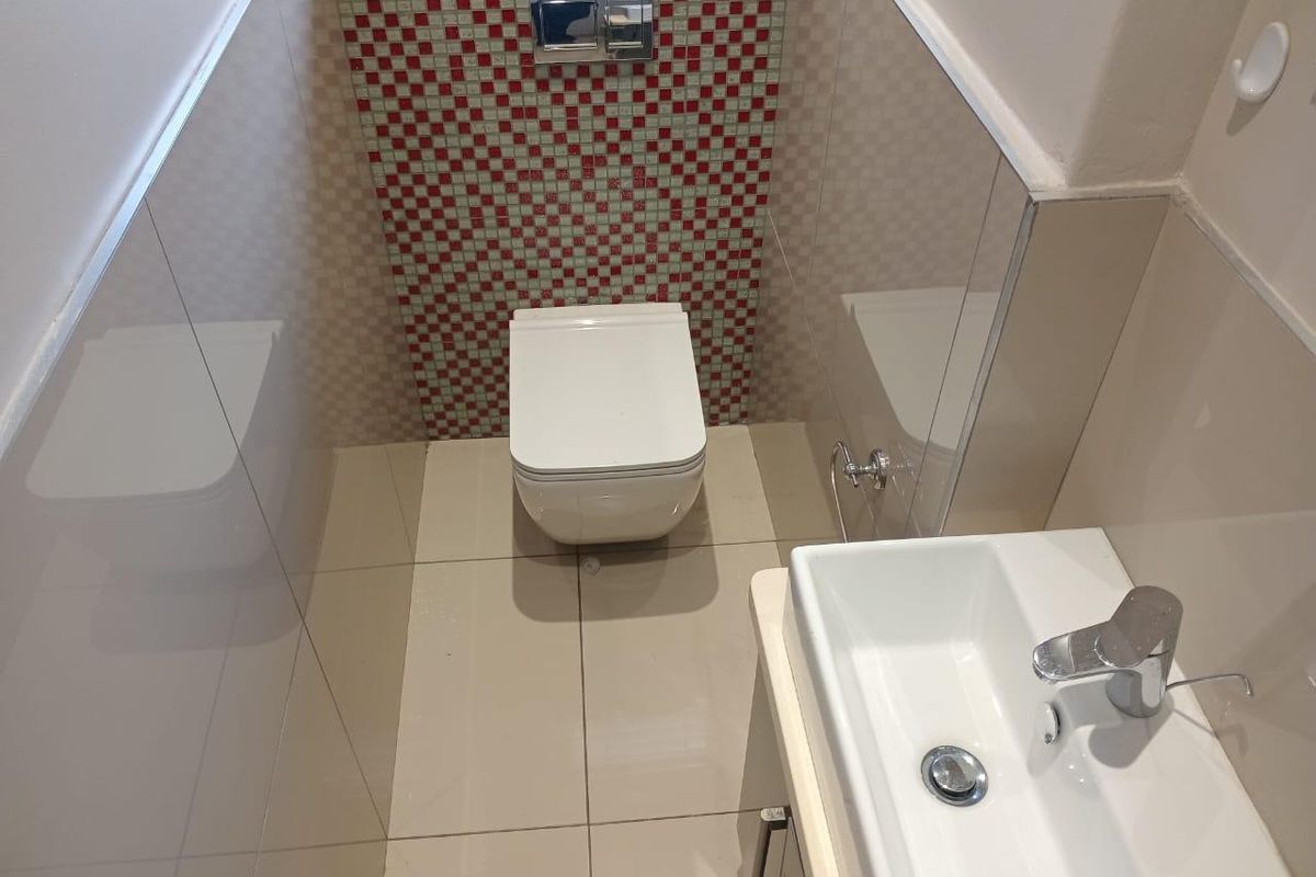 A compact bathroom featuring a wall-mounted toilet with a mosaic tile feature wall, tiled flooring, and a modern wall-mounted basin.