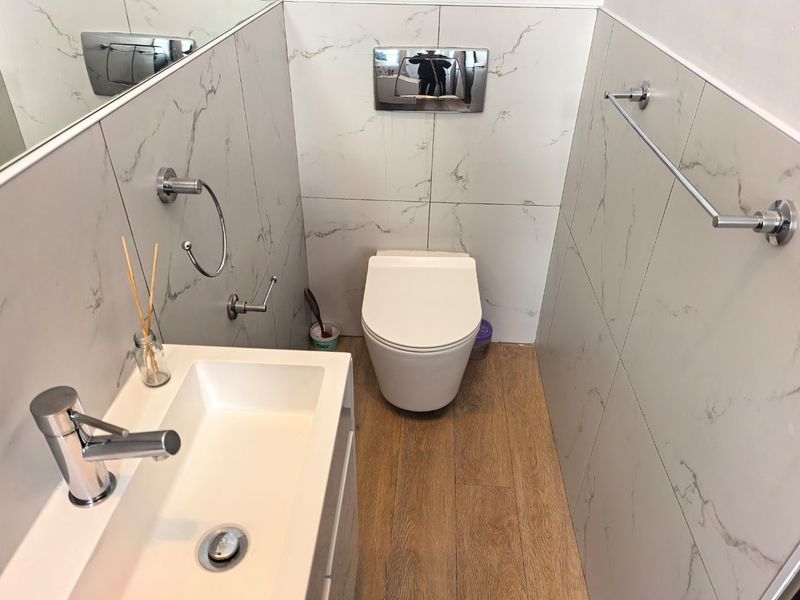 Modern bathroom featuring marble-effect wall tiling, wood-look flooring, a wall-mounted toilet with a concealed cistern, and a sleek vanity basin.