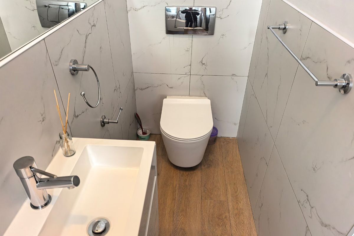 Modern bathroom featuring marble-effect wall tiling, wood-look flooring, a wall-mounted toilet with a concealed cistern, and a sleek vanity basin.