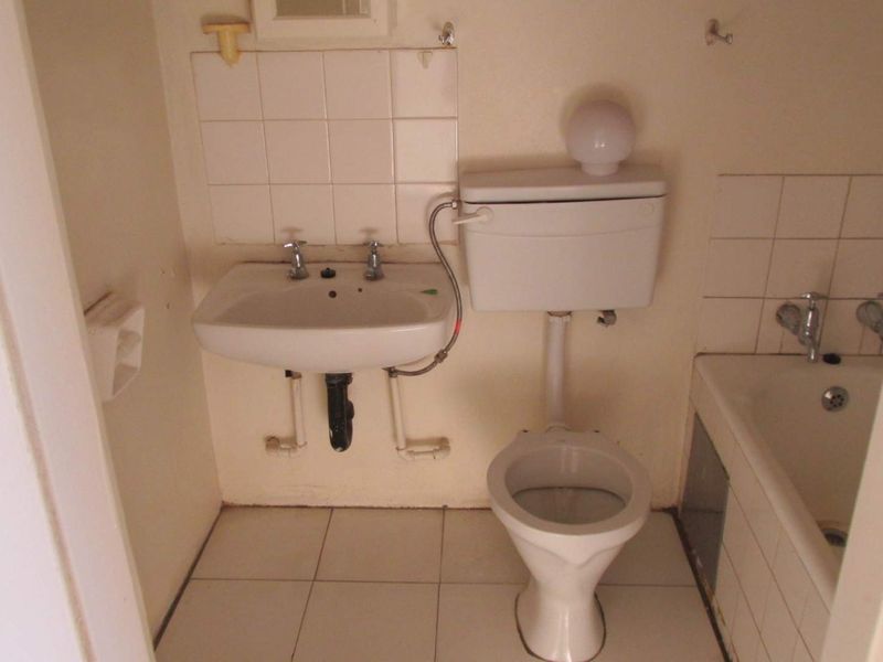 A compact, dated bathroom featuring a wall-mounted basin, standard toilet, and bathtub with tiled splashbacks, requiring modernization of finishes and fixtures.