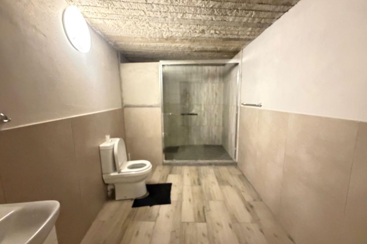 A functional bathroom featuring a walk-in shower with a glass enclosure, tiled flooring, and wall cladding, with an unfinished ceiling finish.