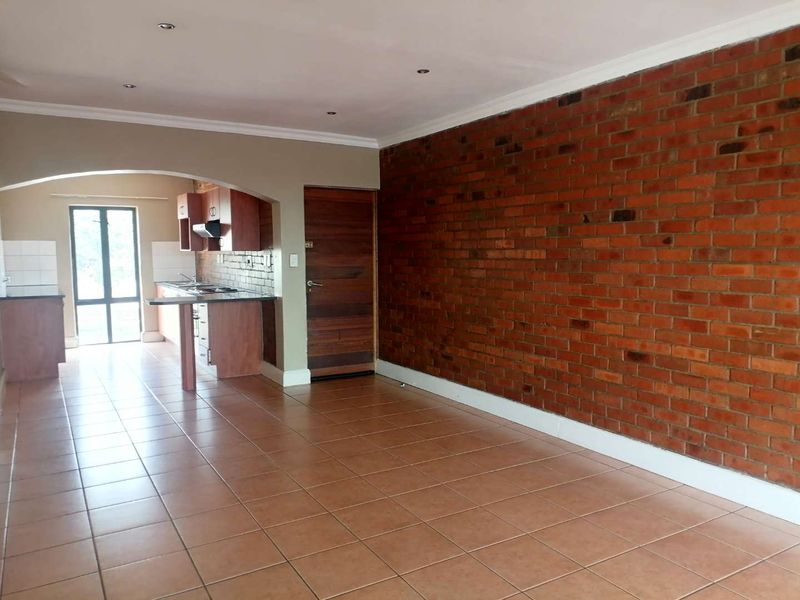 Open-plan living area featuring an exposed brick feature wall, tiled flooring, and an adjoining kitchen with built-in cabinetry and an extractor fan.