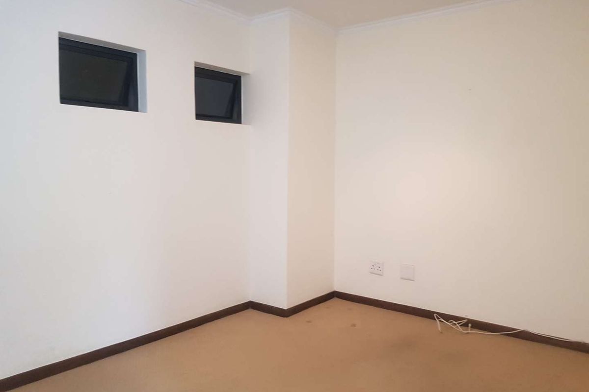 A vacant bedroom featuring neutral walls, carpeted flooring, and two high-set windows providing natural light.