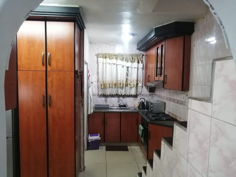 A functional kitchen featuring built-in wooden cabinetry, a double sink, integrated hob, and extractor fan with tiled splashbacks and flooring.