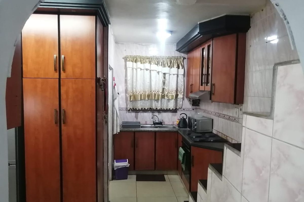 A functional kitchen featuring built-in wooden cabinetry, a double sink, integrated hob, and extractor fan with tiled splashbacks and flooring.