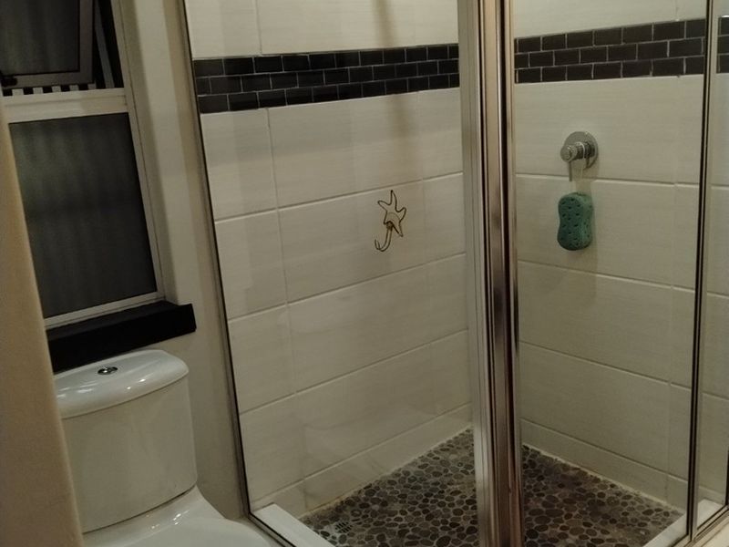 A clean bathroom featuring a glass-enclosed shower with pebble flooring, white wall tiles with a dark accent border, and a standard toilet.