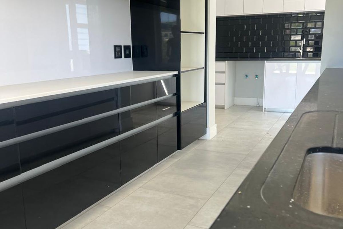 Modern kitchen featuring high-gloss black cabinetry, stone countertops, and a seamless transition into a secondary scullery area with white cabinetry and subway tile backsplash.