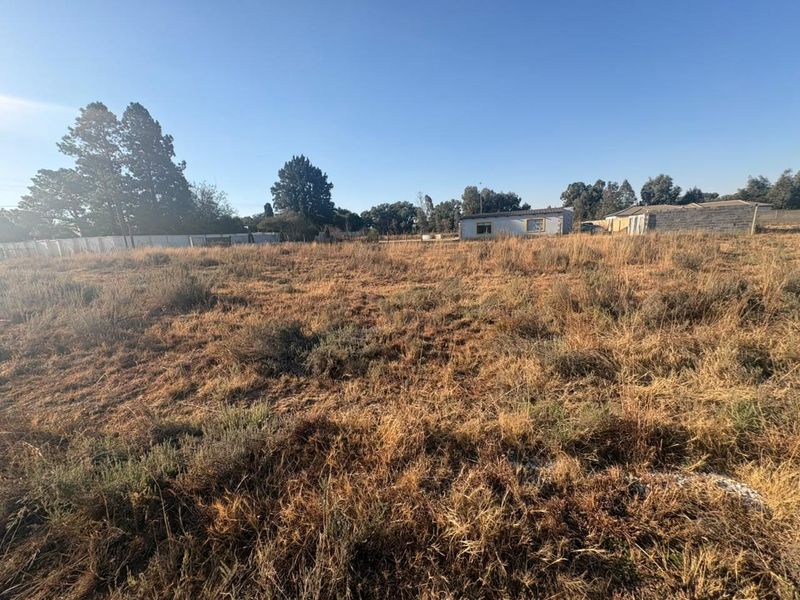 A wide-angle view of a vacant residential plot featuring dry grass and perimeter fencing, suitable for future development.
