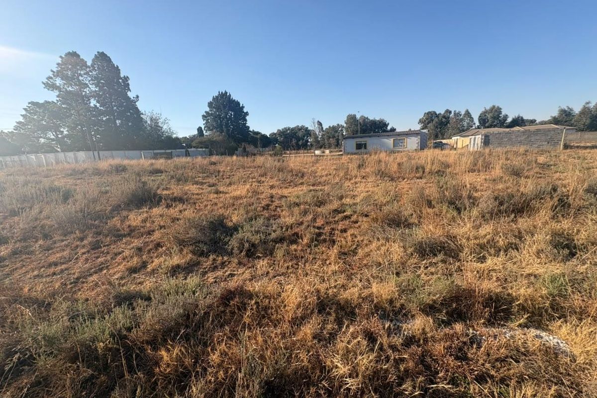 A wide-angle view of a vacant residential plot featuring dry grass and perimeter fencing, suitable for future development.