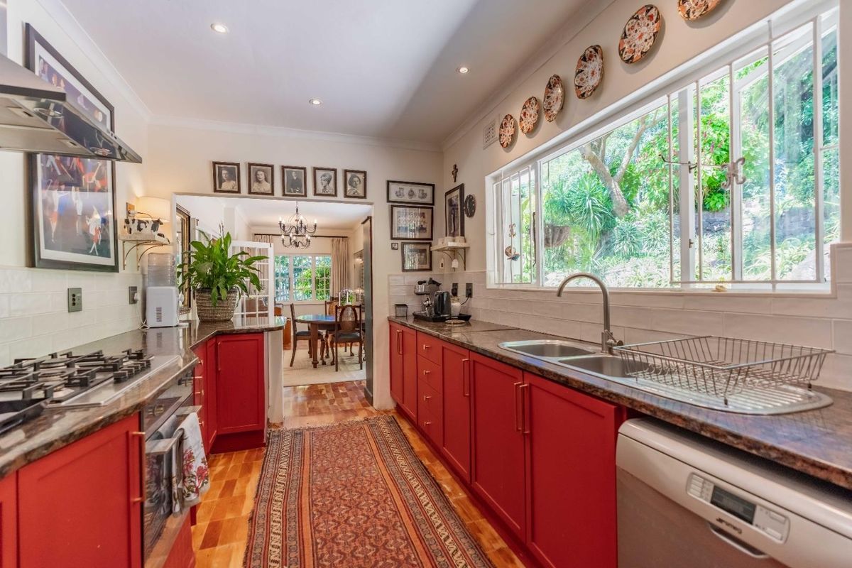 A well-maintained kitchen featuring vibrant red cabinetry, granite countertops, a gas hob, and a large window overlooking the garden, with an adjacent dining area.
