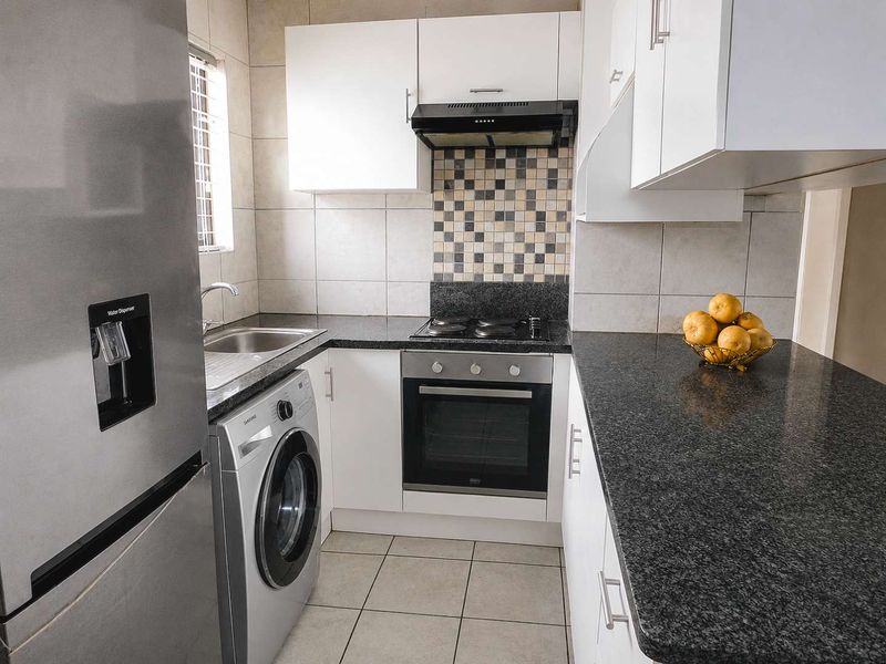 Compact kitchen featuring white cabinetry, dark granite countertops, tiled backsplash, and integrated appliances including an oven, hob, and extractor fan.
