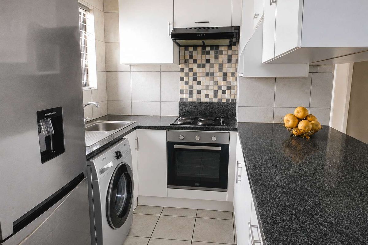 Compact kitchen featuring white cabinetry, dark granite countertops, tiled backsplash, and integrated appliances including an oven, hob, and extractor fan.