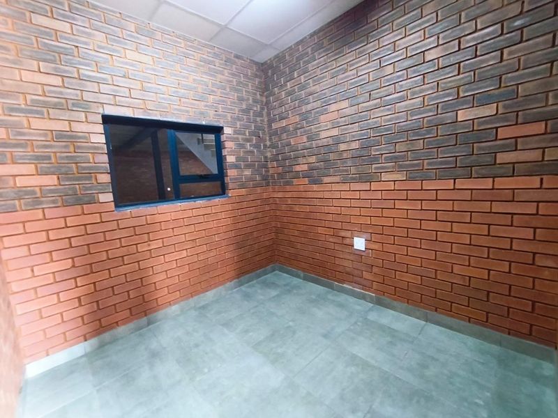 A clean, empty office space featuring exposed brick walls, tiled flooring, and a modern aluminium window frame.