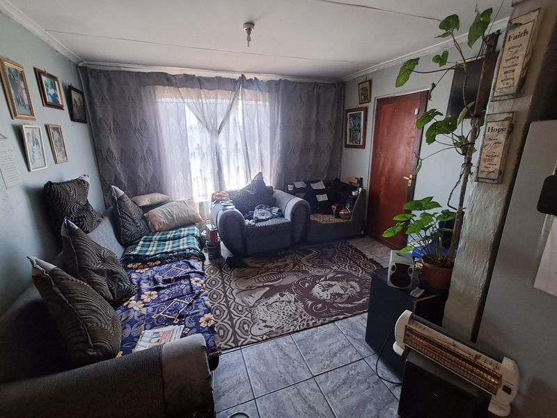 A compact living room featuring tiled flooring and a timber door, requiring cosmetic updates to improve the overall aesthetic and condition of the space.