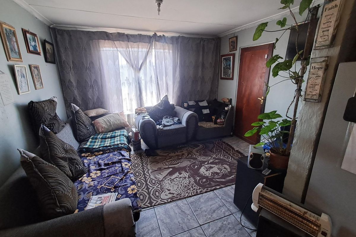 A compact living room featuring tiled flooring and a timber door, requiring cosmetic updates to improve the overall aesthetic and condition of the space.